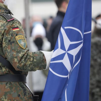 En soldat med Tysklands flagga och ett Nato-märke på armen håller i Natos flagga. 