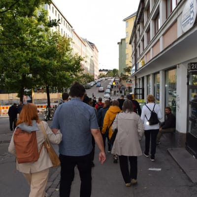 En grupp människor går nerför en gata i Sörnäs, deltar i en guidad rundtur som leds av Pertti Stenman.