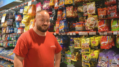 En man i röd skjorta står framför en butikshylla med godis.