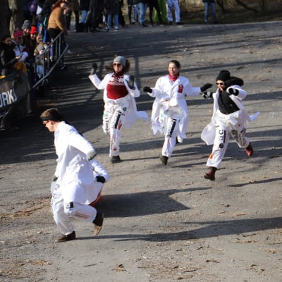 Fyra vitklädda personer springer ner för backen i full fart.