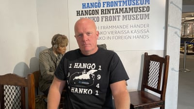 Man sittande vid träbord med en vaxdocka i bakgrunden.