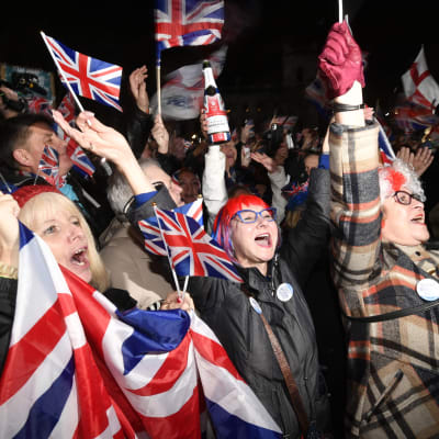 En folkmassa jublar och viftar med Storbritanniens flaggor, tre glada damer i förgrunden med händerna i luften.