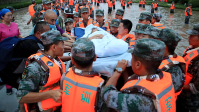 En patient från ett sjukhus i Henan bärs över översvämmade gator på en bår av räddningsmanskap.