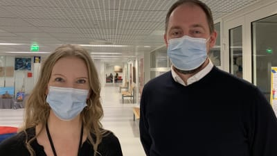 En kvinna och en man står i skolkorridor, bägge bär munskydd.