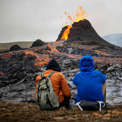Tre personer som sitter och tittar på vulkanutbrottet på Island
