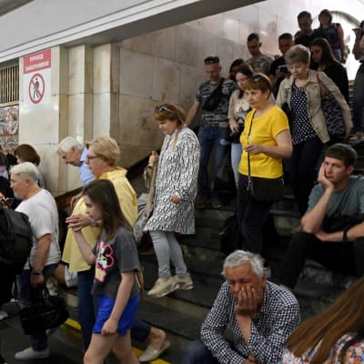Ihmiset kulkevat metroaseman portaissa. Osa istuu portailla ja nojaa käteen.