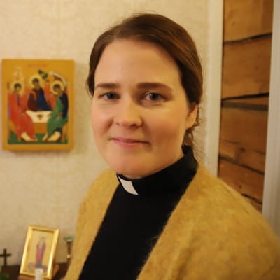 Mari Leppänen, en dam med mörkt hår bakåtkammat i hästsvans, gul tröja och en svart dräkt med prästkrage.