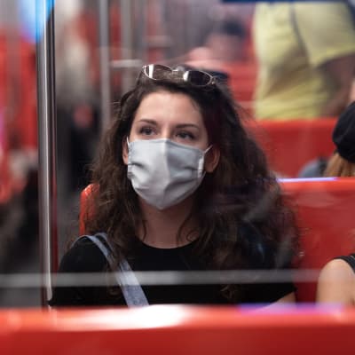 Nainen istuu metrossa maski päässään.