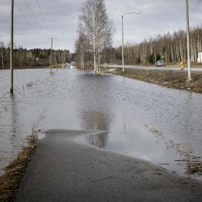En cykelväg översvämmad av vatten, till höger i bilden syns en riksväg med biltrafik.