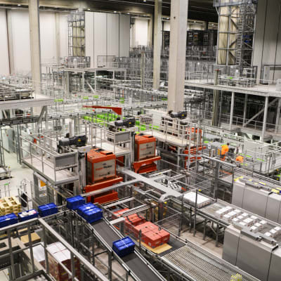 Vy inifrån logistikcentral. En massa rullband och produkter som åker förbi samt några arbetare i orange kläder synns.