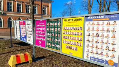 Valaffischer på rad framför ett orange stenhus.