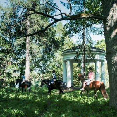 Kolme ratsukkoa matkalla metsän halki, ohittavat 1800-lukulaisen huvimajan. 