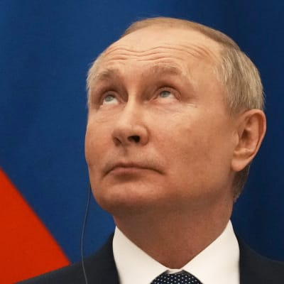 En man i kostym, Rysslands president Vladimir Putin, tittar uppåt framför en rysk flagga.