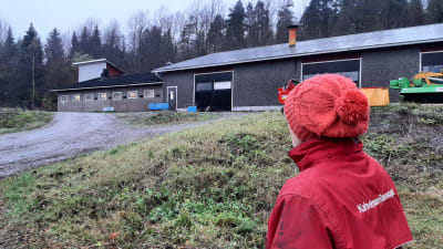 Anne-Maj Blomqvist står med ryggen mot kameran framför gårdens svinhus. 