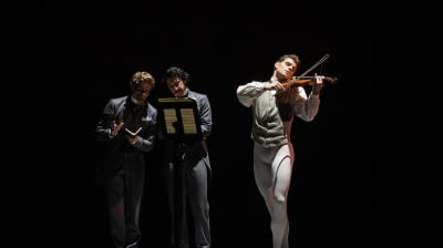 En man som spelar på en violin och tvä män som står böjda över ett notställ.