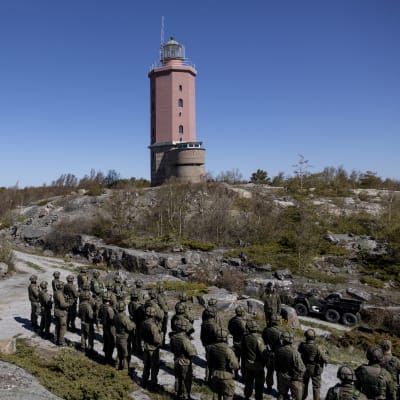 Sotilasrivistön edessä Merivoimien komentaja Jori Harju käsi lipassa. Taustalla kallioinen saari ja punainen Russarön majakka. 