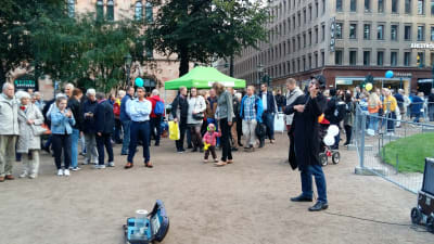 I Esplanadparken står det gatumusikanter eller andra artister, parken är full med folk.