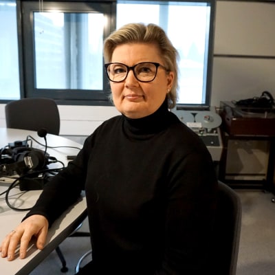 Kvinna i svart polotröja och glasögon sitter i en radiostudio.
