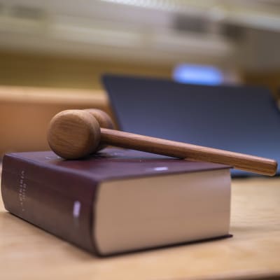 En klubba ligger över en lagbok på ett bord i en tingsrättssal. 