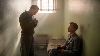 stående man i en liten fängelsecell med en sittande man framför sig