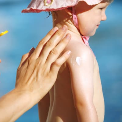 En person sätter på solkräm på ett barn.