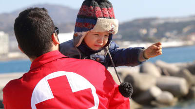 Röda Korset-medarbetare hjälper en flyktingpojke som anlänt till Kreta i Grekland.