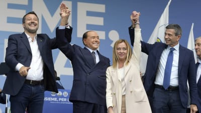 Fyra italienska politiker står på scen och håller i varandras händer och ler.