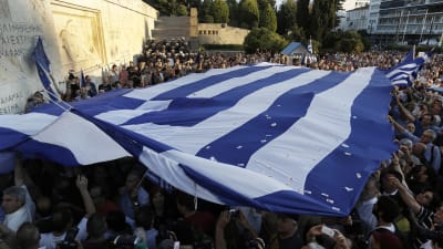 Demonstranter som vill att Grekland stannar kvar i EU håller upp den grekiska flaggan utanför parlamentet i Aten.