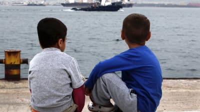 Två pojkar sitter vid havet utanför ett flyktingläger i Grekland.