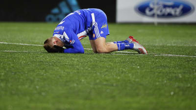 Fotbollsspelare ligger på marken och håller sig för ansiktet.