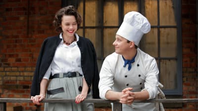 Karaktärerna Nina och Calle står på restaurangens bakgård och ler åt varandra.