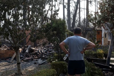 En man tittar på ett nedbrunnet hus efter en skogsbrand i Varybobi i Grekland.