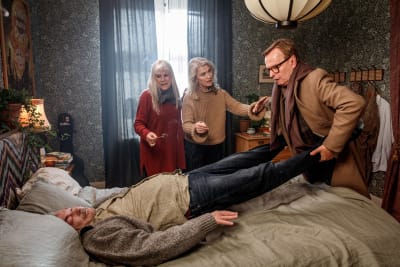 Tre personer försöker flytta på sin döde vän som ligger på en säng. Scen ut dramakomedin Äntligen!