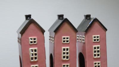 Tre rosafärgade hus i porslin står i rad på ett träbord.