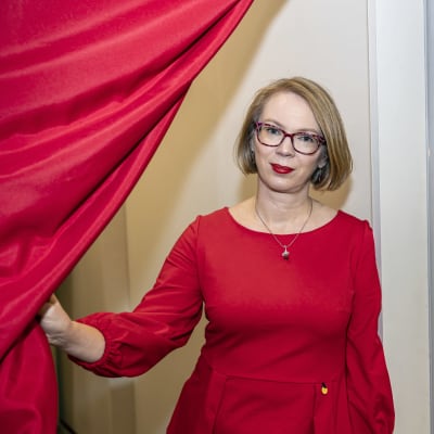 Maria Turtschaninoff tittar fram bakom en röd gardin i ett rum intill bokmässans utställningsutrymmen. 