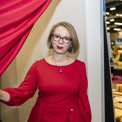 Maria Turtschaninoff tittar fram bakom en röd gardin i ett rum intill bokmässans utställningsutrymmen. 