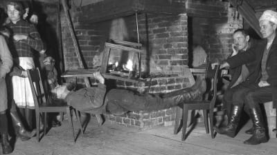 En man leker "ligga lik", där man håller kroppen så styv som möjligt och håller sig vågrätt mellan två stolar. Bilden är tagen 1935 i Bromarf.