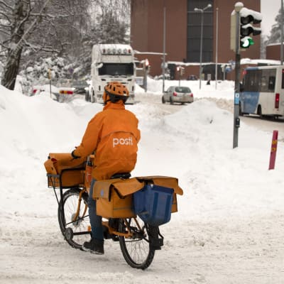 Postinjakaja pyöräilee talvisessa katumaisemassa.