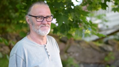 Frank Holmlund i grå tröja står vid ett träd.
