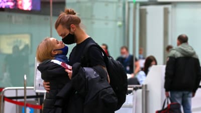 En man och en kvinna iklädda munskydd kramas i en flygterminal. 