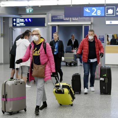 Flygpassagerare med ansiktsskydd drar sitt bagage på flygplatsen.