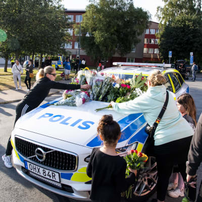 Människor lägger blommor på en polisbil i Göteborg
