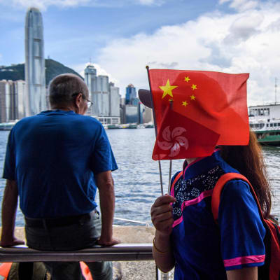 Invånare med Hongkong i bakgrunder som håller upp en kinesisk flagga. 