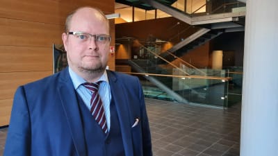 Skallig man med glasögon blå kostym och slips.