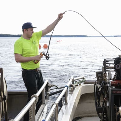 Keltapaitainen kalastaja vetää verkkoa kaarelle kalastusveneen kyydissä.