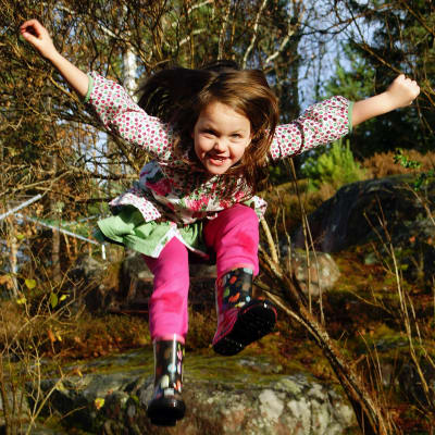 En leende flicka hoppar i skogen.