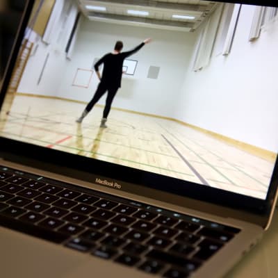 tietokoneen näytöllä video, jossa opettaja näyttää tanssikuviot tyhjässä jumppasalissa