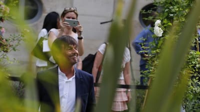 Frankrikes nya miljöminister Nicolas Hulot går bland växter och ser glad ut. I bakgrunden syns en kvinna som fotograferar honom.