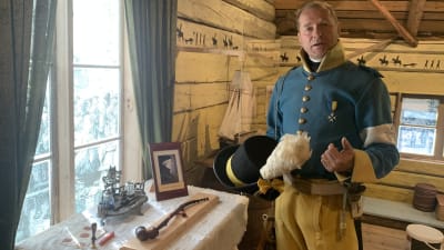 En man i historisk uniform står i ett museum med artefakter