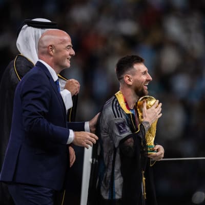 Lionel Messi kävelee MM-pokaali sylissään. Fifan puheenjohtaja Gianni Infantino ja Qatarin emiiri Tamim bin Hamad Al Thani katsovat perään.